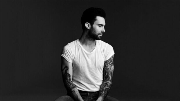 Adam Levine Wallpapers shows a man with detailed tattoos on both arms sitting against a dark background, HD Desktop Wallpaper