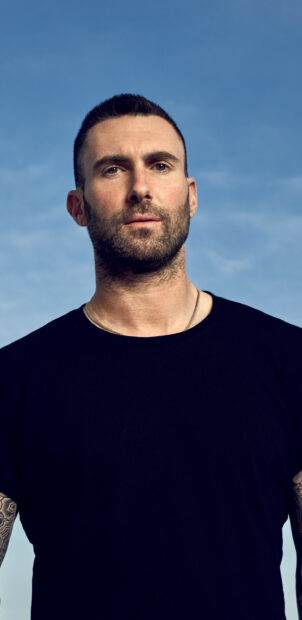 Adam Levine stands outdoors with a focused expression against a clear sky, 2K Mobile Wallpaper
