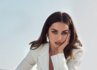 Elegant woman in white blazer and pants, posing outdoors with mountain scenery, showcasing fashion and style.
