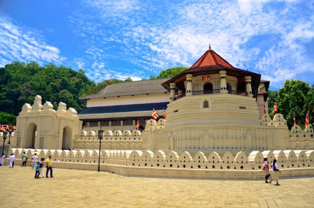 The ancient temple in Sri Lanka stands with flags and visitors under a bright blue sky, 2K Desktop Wallpaper