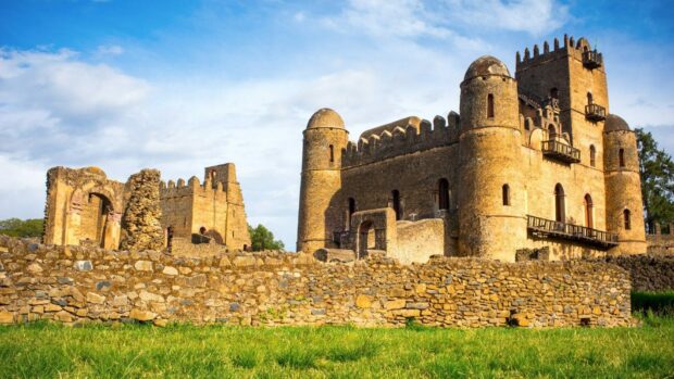 The ancient castle in Ethiopia stands tall under a bright sky with green grass in front, HD Desktop Wallpaper