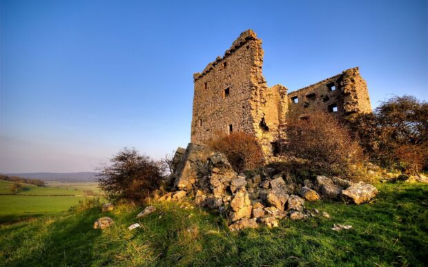The ancient castle ruins stand tall on a grassy hill under a clear blue sky in Northern Ireland, 2K Desktop Wallpaper
