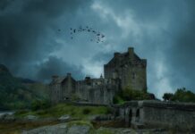 Medieval stone castle under dark stormy sky with flock of birds flying overhead.