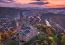 An ancient stone church sits on a hill surrounded by autumn trees and overlooking a Bulgarian town