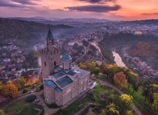 An ancient stone church sits on a hill surrounded by autumn trees and overlooking a Bulgarian town