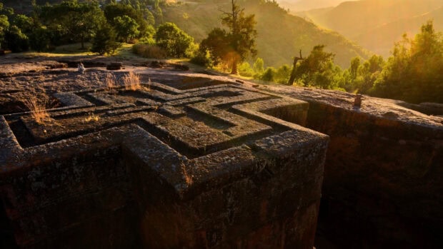 A carved rock church surrounded by trees and hills in Ethiopia during sunset, 2K Desktop Wallpaper