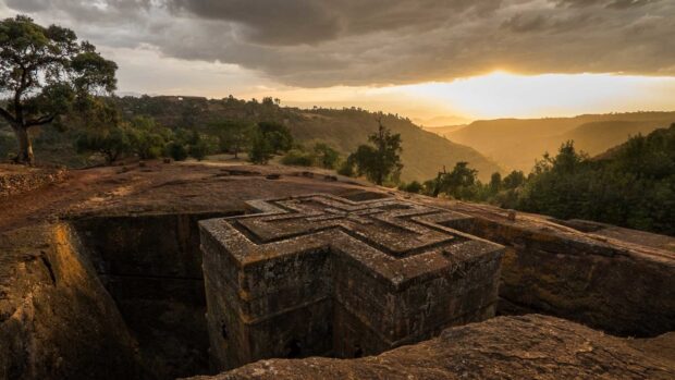 A historic rock hewn church is surrounded by hills under a cloudy sky in Ethiopia, HD Desktop Wallpaper