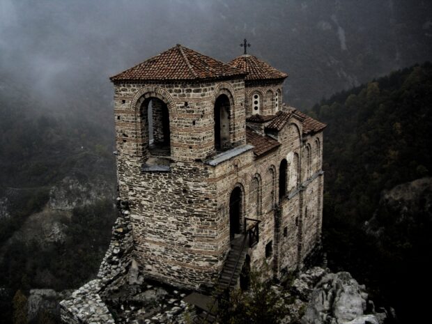An old stone church stands on a rocky cliff surrounded by mountains in Bulgaria, HD Desktop Wallpaper