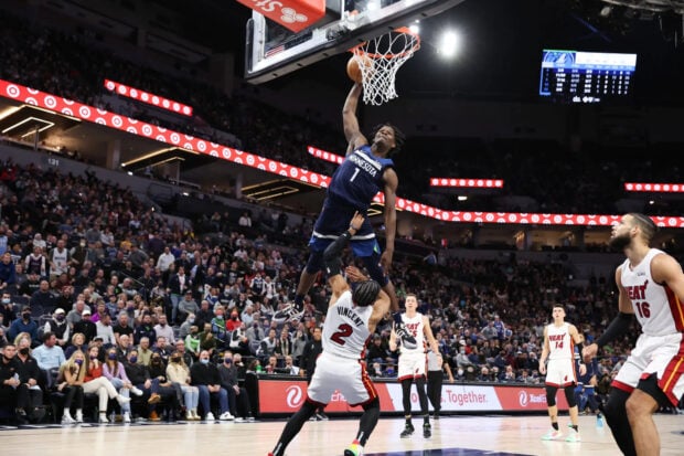 Anthony Edwards soaring above a defender during a basketball game in an arena filled with fans