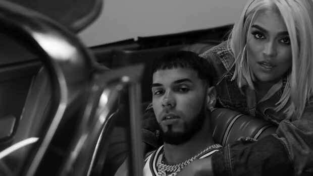 Anuel Aa and a woman pose inside a car with serious expressions in this black and white image