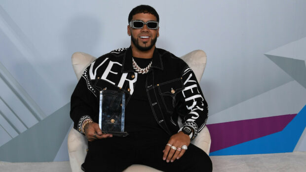 Anuel Aa is smiling while holding a clear award seated on a white chair, HD Desktop Wallpaper