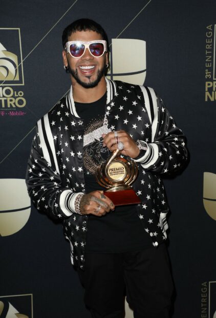 Anuel Aa is smiling while holding a Premio Lo Nuestro award in a star patterned jacket, Desktop Wallpaper