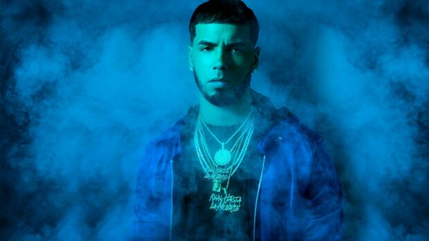 Anuel Aa is standing surrounded by blue smoke wearing chains and a blue jacket, 2K Desktop Wallpaper