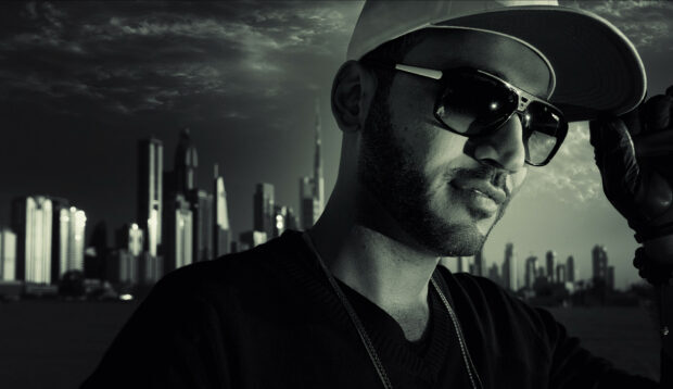 Anuel Aa is posing with sunglasses and cap against a city backdrop, HD Desktop Wallpaper