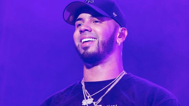 Anuel Aa is smiling on stage with purple lighting and wearing chains, 2K Desktop Wallpaper