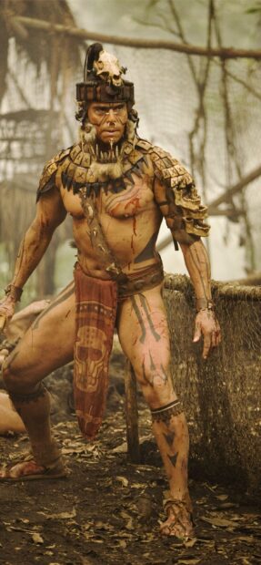 Một chiến binh bộ lạc từ Apocalypto mặc trang phục sơn truyền thống và đội mũ bảo hiểm hình đầu lâu trong bối cảnh rừng, Hình nền điện thoại 2K
