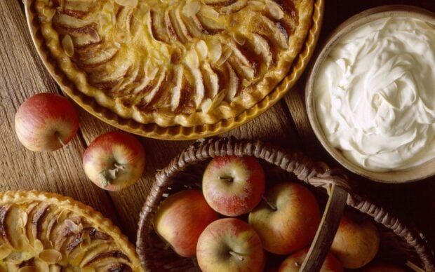 A delicious apple pie with fresh apples and a bowl of cream on a wooden table, HD Desktop Wallpaper