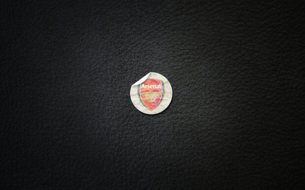 A crumpled Arsenal Fc logo sticker on a black textured background