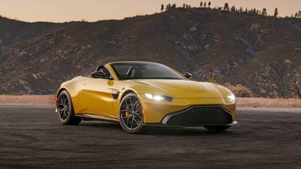Yellow Aston Martin sports car parked on asphalt with mountain background