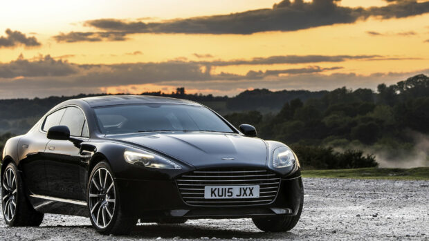 A sleek Aston Martin sports car parked outdoors during a sunset with trees in the background