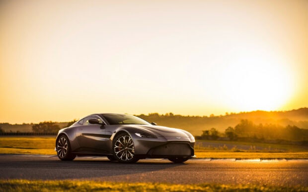 Aston Martin sports car parked on a racetrack during a golden sunset