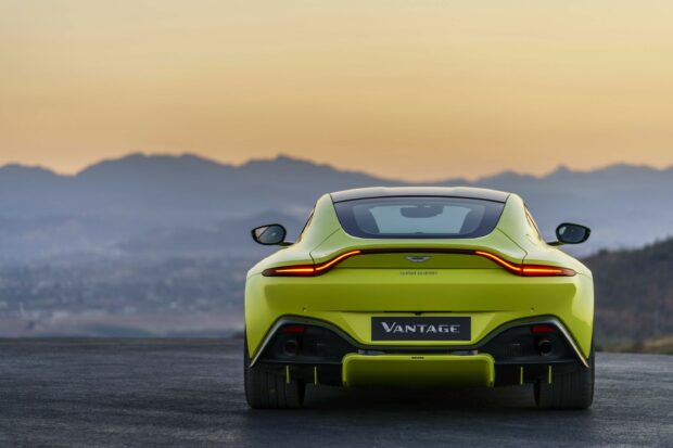 Rear view of a bright yellow Aston Martin car on the road with mountains in the background