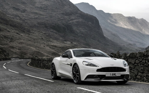 A white Aston Martin car parked on a mountain road with rocky hills in the background