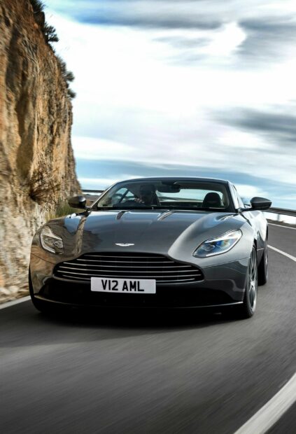 Aston Martin car driving fast on a mountain road with rocky cliffs and cloudy sky