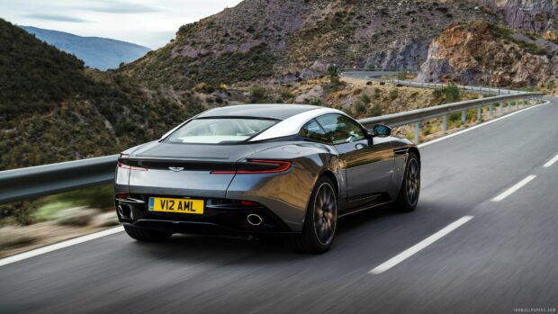 A sleek Aston Martin car driving on a mountain road surrounded by rocky hills