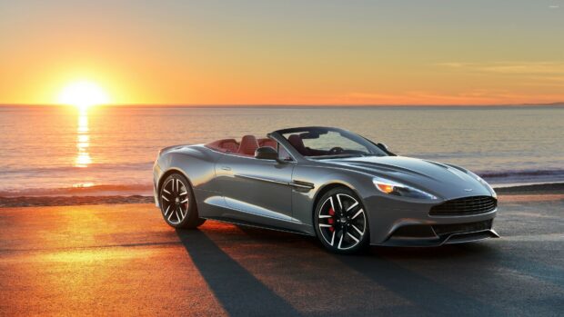 Aston Martin convertible sports car parked by the ocean at sunset with a vibrant sky