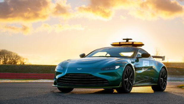 Green Aston Martin car on racetrack during sunset with bright sky and track lights