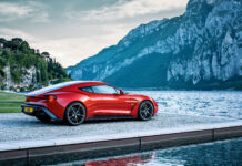 Red Aston Martin sports car parked near the lake with mountains in the background