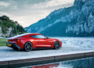 Red Aston Martin sports car parked near the lake with mountains in the background