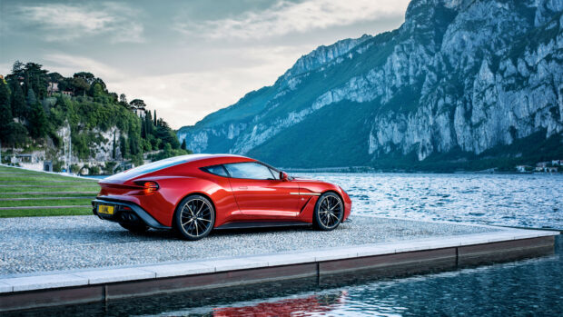 Red Aston Martin sports car parked near the lake with mountains in the background