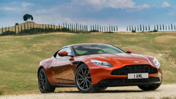 A sleek Aston Martin car parked on a dirt road with a scenic countryside background