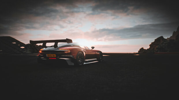 A sleek Aston Martin car with a large rear wing parked on an empty road at sunset