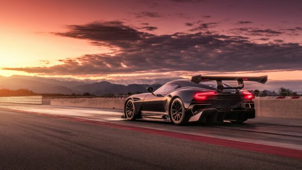 A sleek Aston Martin racing car on a track during sunset with mountains in the background