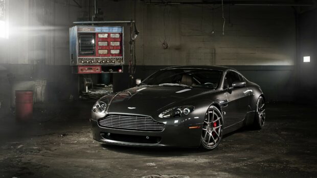 A sleek Aston Martin sports car parked inside an old garage with industrial equipment nearby