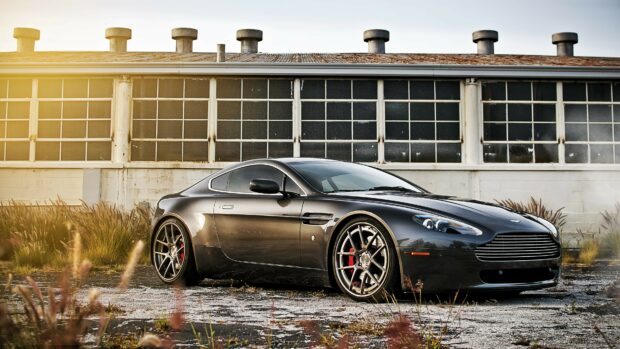 A sleek Aston Martin parked in front of an industrial building with large windows