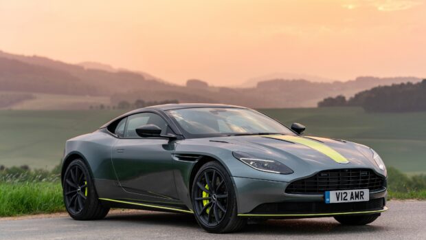 A sleek Aston Martin sports car parked on a road during sunset with a scenic background