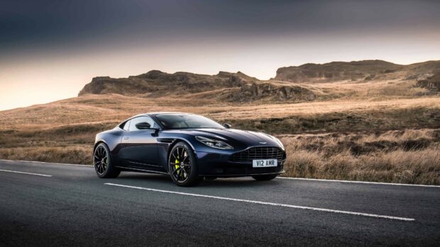A sleek Aston Martin sports car parked on an empty road with hills in the background