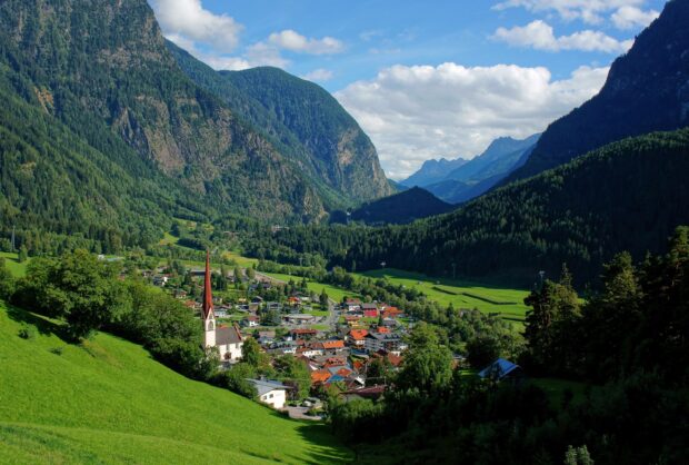 A vibrant Austrian village is nestled among green alpine hills and mountains, 2K Desktop Wallpaper
