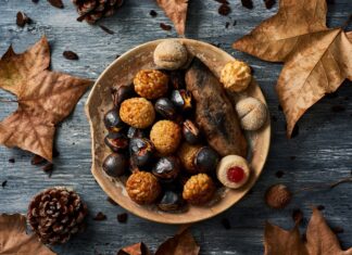 A plate filled with roasted chestnuts and assorted sweet treats surrounded by dry autumn leaves, 2K Desktop Wallpaper
