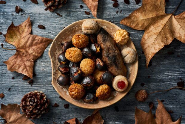 A plate filled with roasted chestnuts and assorted sweet treats surrounded by dry autumn leaves, 2K Desktop Wallpaper