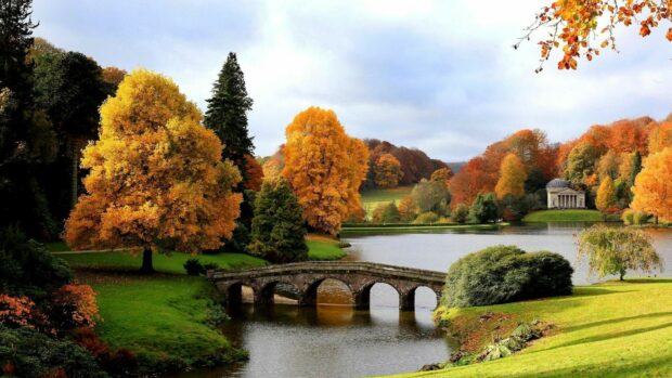 This image of United Kingdom Wallpapers shows a stone bridge over calm water surrounded by autumn trees, HD Desktop Wallpaper