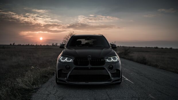 A BMW X5 is parked on a deserted road during sunset with illuminated headlights, 4K Desktop Wallpaper