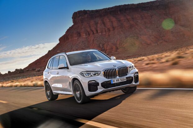 A BMW X5 is driving fast on a desert road with red rock formations in the background, HD Desktop Wallpaper