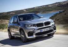 A silver BMW X5 is driving fast on a scenic mountain road near the water, 2K Desktop Wallpaper