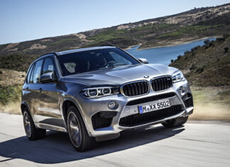 A silver BMW X5 is driving fast on a scenic mountain road near the water, 2K Desktop Wallpaper