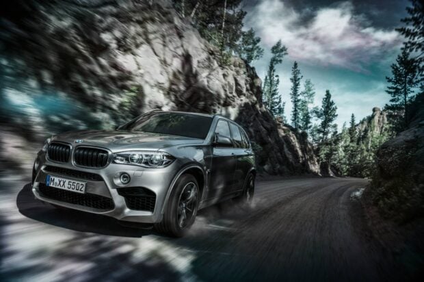 A silver BMW X5 is speeding down a winding mountain road surrounded by trees and rocks, HD Desktop Wallpaper